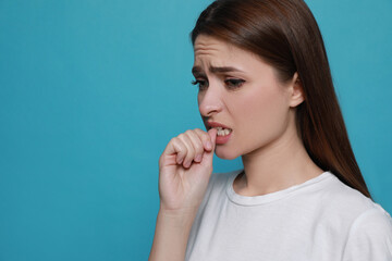 Naklejka premium Young woman biting her nails on light blue background. Space for text