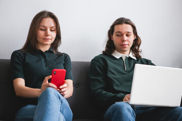 Couple sitting on the sofa with notebook and phone. Man and woman communicating on the electronic gadgets. Social isolation, distant learning students