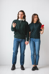 Couple in green shirts holding phones in hands on white background. Young man and woman using phones and laptop. Modern technology