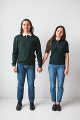 couple standing against a white wall. Students in green shirts on white background. man and woman holding hands