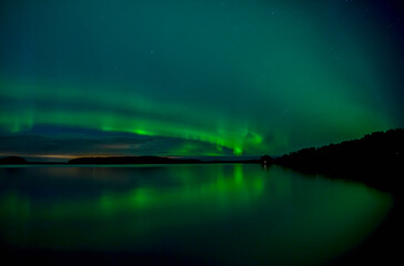 Fototapeta na wymiar Northern lights dancing over calm lake in Farnebofjarden national park in north of Sweden.