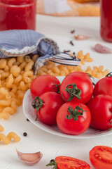 Red cherry tomatoes on a white plate, pasta fusilli, garlic, peper on a white background.