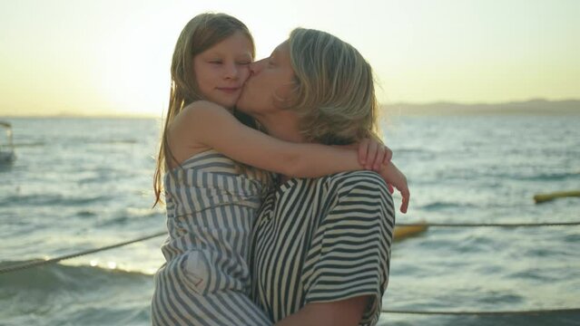 Happy young mother hugging with her child in summer day at sunset - mum kissing her daughter outdoor - Family lifestyle motherhood togetherness and tender moments concept