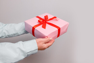 Close up shot of woman hands holding surprise gift package box on pink pastel background with copy space. Valentine's gift