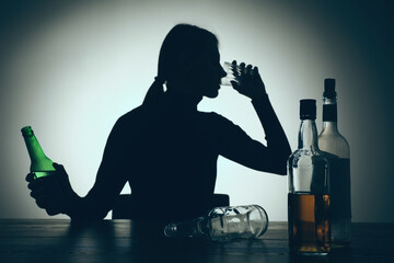 Alcohol addiction. Silhouette of woman drinking beer on wooden table, backlit