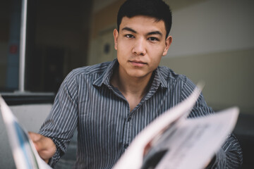 Asian millennial guy reading newspaper on stairs