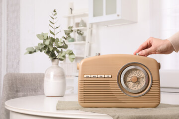Woman turning volume knob on radio indoors, closeup. Space for text