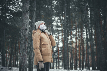 Fototapeta na wymiar A young woman with blond hair in a medical mask walks in the winter forest.