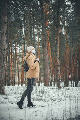 A young girl in winter clothes and in a medical mask walks in the winter forest.