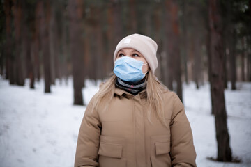 Fototapeta na wymiar Attractive blonde girl in a medical mask is walking in the forest.