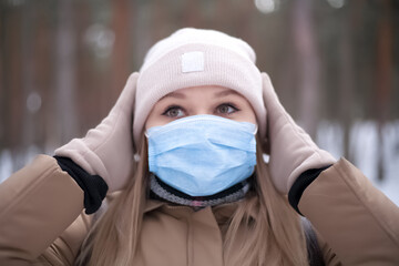A young blonde girl in a medical mask walks in the winter forest.