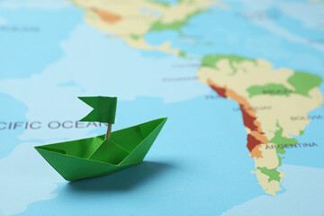 Green paper boat with flag on world map. Space for text