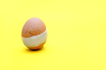 A broken egg with a crack and medical tape glued to it. The concept of treatment and healthcare. Medical plaster on a broken chicken egg on a yellow background. Free space for text