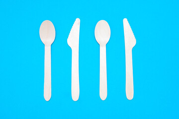 Wooden spoons and knives on a blue background. Eco-friendly tableware in the form of two spoons and two knives. Disposable eating utensils close-up