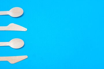 Wooden spoons and knives on a blue background. Eco-friendly tableware in the form of two spoons and two knives with free space for text and advertising. The concept of ecological disposable tableware