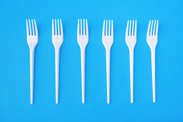 Fototapeta na wymiar Six plastic forks on a blue paper background for single use. Dangerous plastic for the environment. Disposable eating utensils