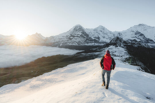 Man in the snow admiring Eiger, Monch and Jungfrau peaks at dawn, Mannlichen, Jungfrau Region, Bern Canton, Swiss Alps, Switzerland
