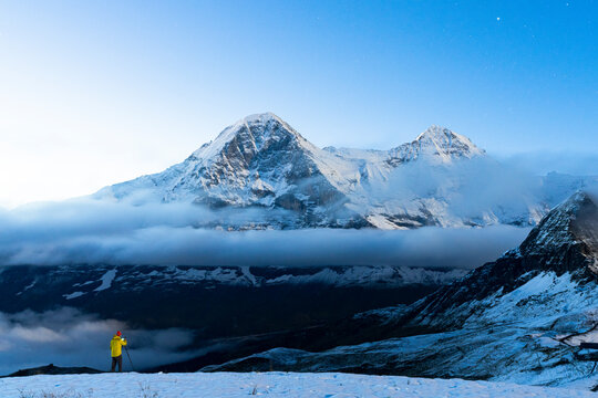 Man with tripod in the snow photographing Eiger and Monch mountain peaks at night, Mannlichen, Bern Canton, Swiss Alps, Switzerland - Powered by Adobe