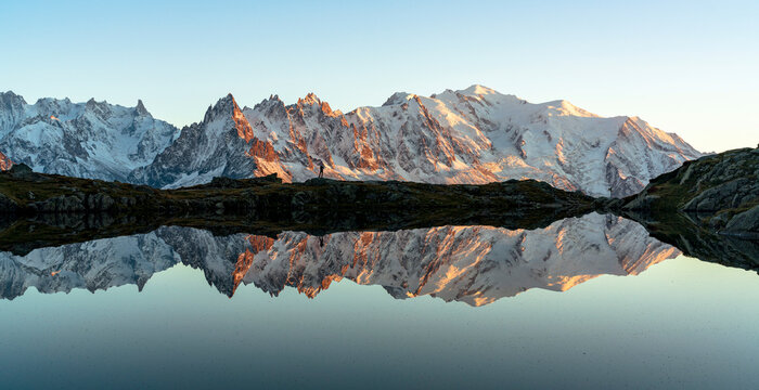 Hiker admiring Dent du Geant and Mont Blanc covered with snow reflected in Lacs des Cheserys at sunset, Haute Savoie, French Alps, France