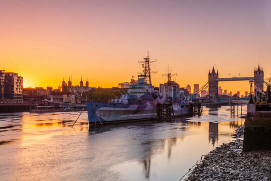 HMS Belfast and Tower Bridge at sunrise with a low tide on the River Thames, London, England