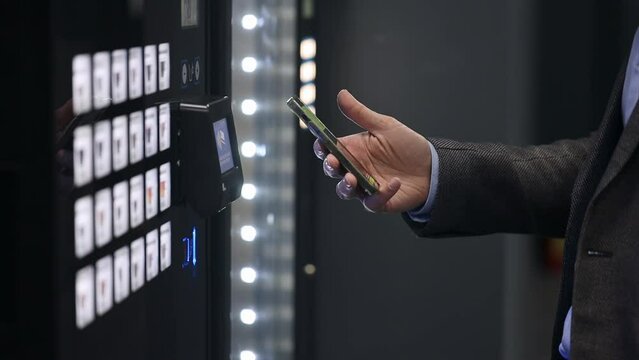 A man puts his smartphone to the sensor of an electronic coffee machine, tries to buy coffee, pay for coffee with a credit card from his phone, close-up.