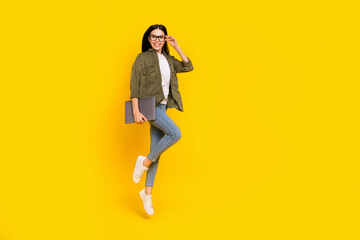 Fototapeta na wymiar Full size photo of funny young lady jump hold laptop wear eyewear shirt jeans footwear isolated on yellow background