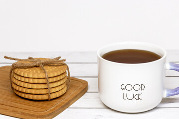 A cup of tea with the inscription good luck and a stack of crispy cookies on a wooden cutting board. Close-up.
