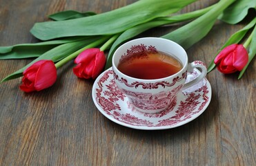 reading over tea. Tea in a beautiful tea pair English porcelain, red book  and red tulips on a dark background. Soft focus