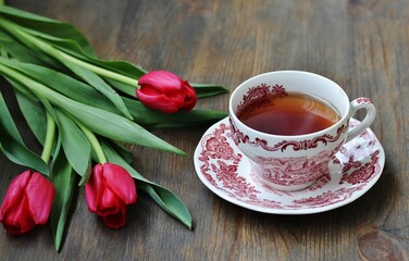 reading over tea. Tea in a beautiful tea pair English porcelain, red book  and red tulips on a dark background. Soft focus