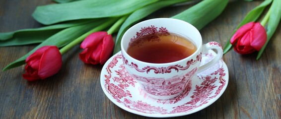 reading over tea. Tea in a beautiful tea pair English porcelain, red book  and red tulips on a dark background. Soft focus