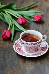 reading over tea. Tea in a beautiful tea pair English porcelain, red book  and red tulips on a dark background. Soft focus