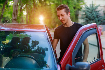 A young man or adult guy driver gets into the car. Background with copy space