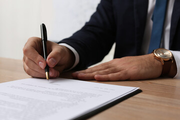 Businessman signing contract at wooden table indoors, closeup