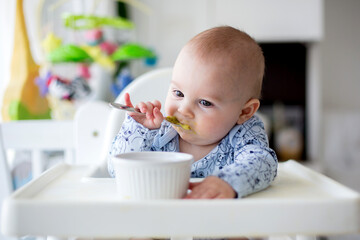 Cute little baby boy, eating mashed vegetables for lunch, mom feeding him