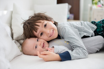 Two children, baby and his older brother in bed in the morning, playing together