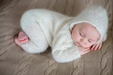 Beatiful baby boy in white knitted cloths and hat, sleeping
