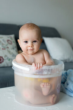 Cute little four month old baby boy, playing in bucket full with water