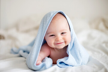 Cute little baby boy, relaxing in bed after bath, smiling happily - obrazy, fototapety, plakaty