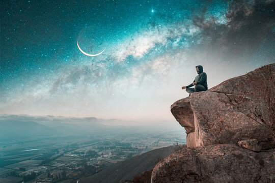 person sitting on the top of the mountain meditating with Milky Way and Moon background