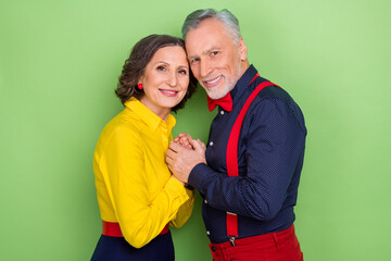 Profile portrait of two aged partners hold hands beaming smile look camera isolated on green color background