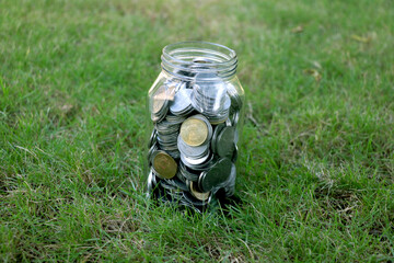 Fototapeta premium glass jar full of coins on green grass background