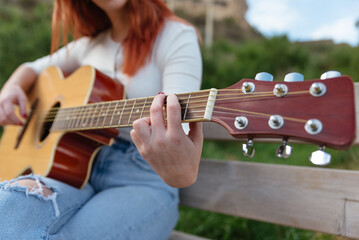 red-haired young woman plays the guitar outdoors sitting .