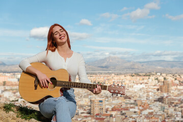 red-haired young woman plays the guitar outdoors sitting .