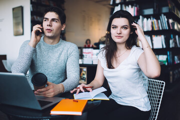 Concentrated young man chatting on smartphone sitting in workspace with colleague