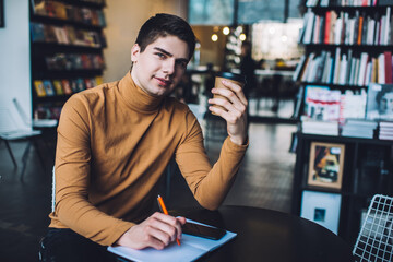 Young man with notebook and cup of coffee to go