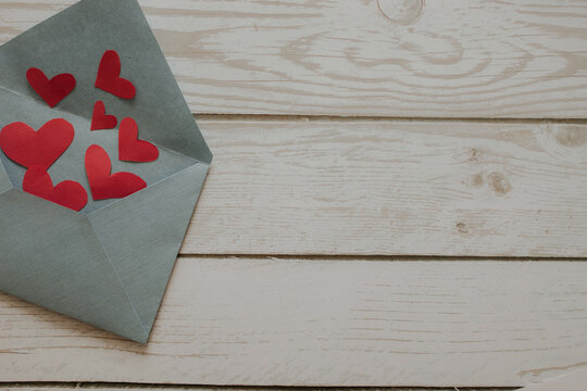 Open envelope with hearts on a wooden background.