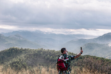 Rear View Of Man With Dog In Backpack Taking Photo High On Mountain