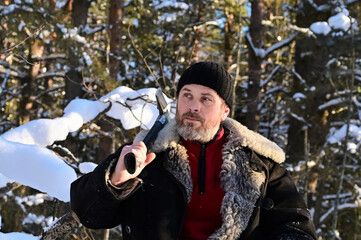 bearded lumberjack in forest with an axe. Portrait of brutal man in snowy winter forest. Logger is...