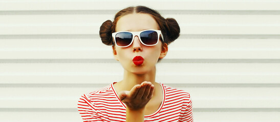 Portrait of young woman blowing her lips sending sweet air kiss with red lipstick wearing striped...