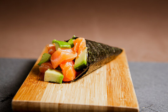 
Sushi temaki freshly prepared with salmon and avocado. Japanese food in a wooden background. Fish and avocado slices. Top view with Copy Space.